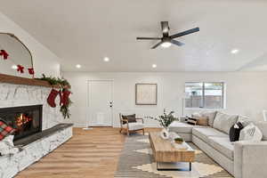 Living room with recessed lighting, light wood-style flooring, a premium fireplace, a textured ceiling, and a ceiling fan