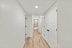 Hall with a textured wall, light wood finished floors, and a textured ceiling