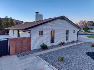Property exterior at dusk with a chimney, brick siding, roof with shingles, and a gate