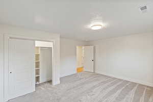 Unfurnished bedroom featuring light colored carpet, a textured ceiling, and a closet