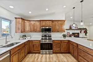 Kitchen featuring appliances with stainless steel finishes, pendant lighting, brown cabinets, light wood finished floors, and a stone fireplace