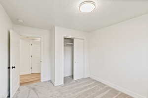 Unfurnished bedroom featuring light carpet, a textured ceiling, and a closet