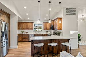 Kitchen featuring stainless steel appliances, a peninsula, decorative light fixtures, a kitchen breakfast bar, and light wood-style flooring