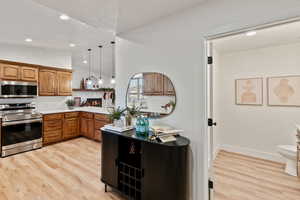 Kitchen with stainless steel appliances, brown cabinetry, decorative light fixtures, light wood-style flooring, and lofted ceiling
