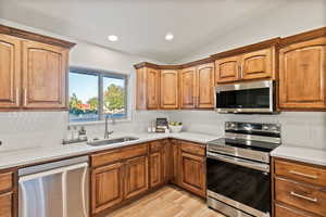 Kitchen featuring stainless steel appliances, tasteful backsplash, brown cabinets, recessed lighting, and vaulted ceiling