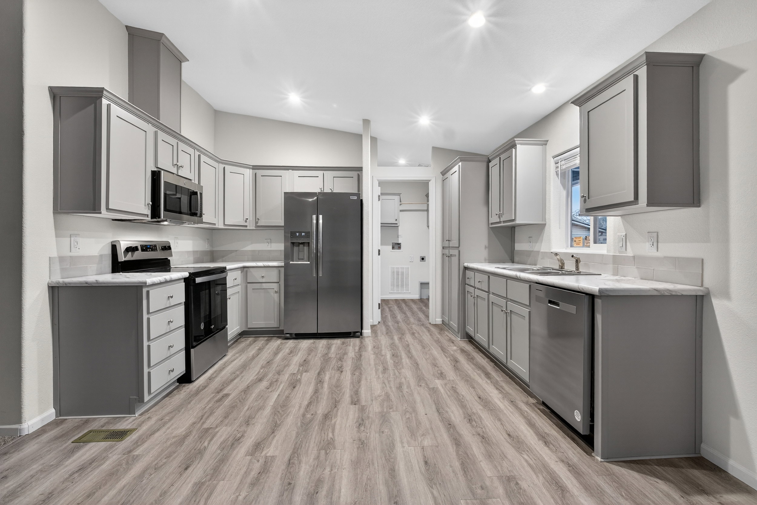 Kitchen featuring gray cabinetry, appliances with stainless steel finishes, lofted ceiling, light wood-style flooring, and recessed lighting