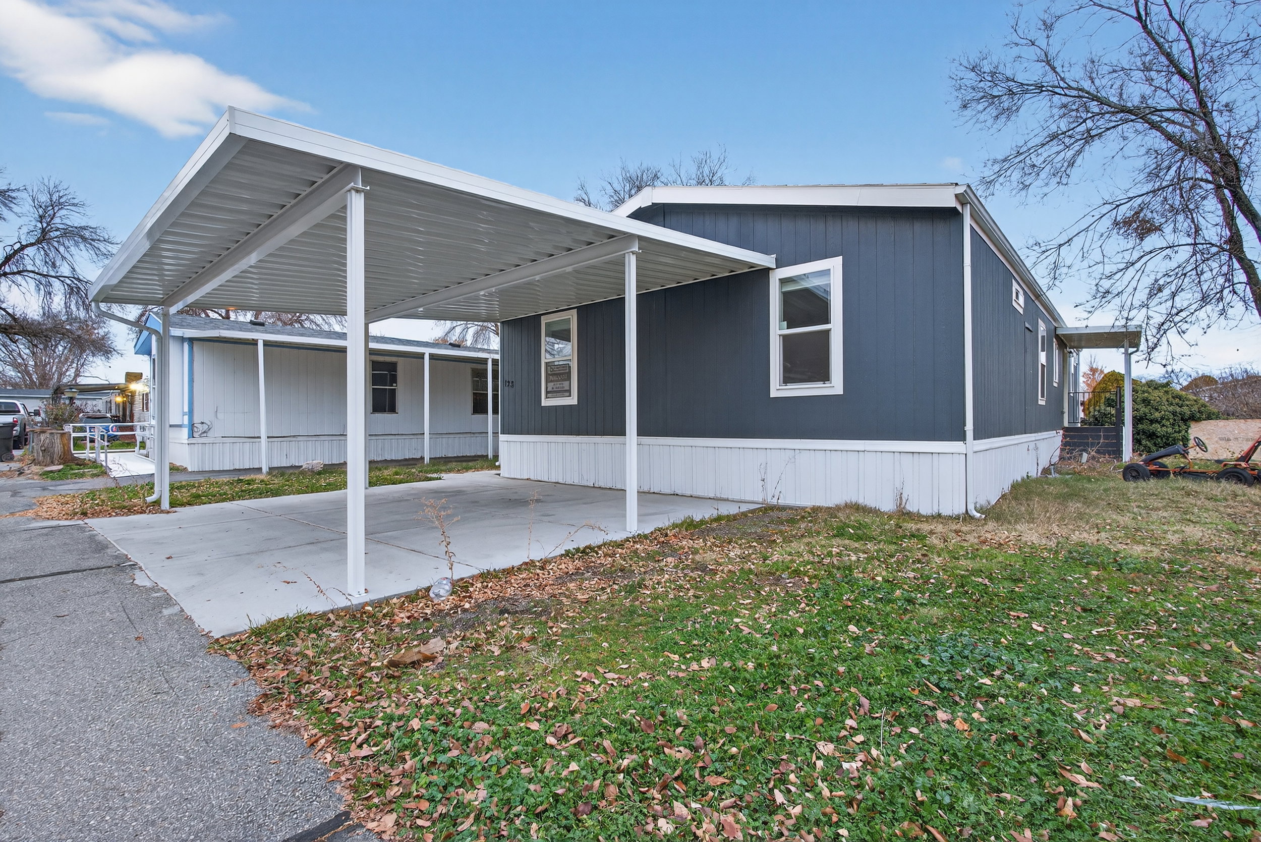 View of front of property featuring a front lawn, a carport, concrete driveway, and a patio