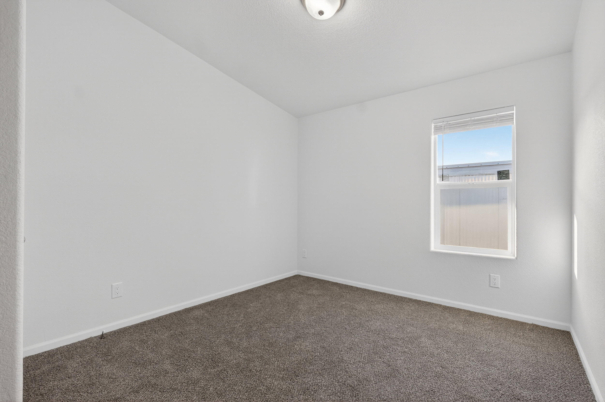 Carpeted empty room featuring baseboards and lofted ceiling