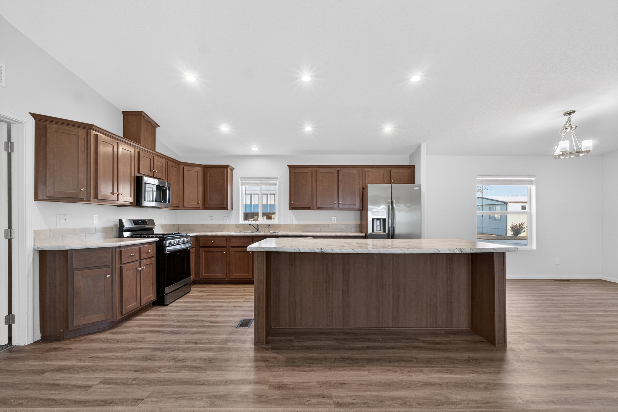 Kitchen featuring appliances with stainless steel finishes, vaulted ceiling, light wood-style flooring, healthy amount of natural light, and a center island