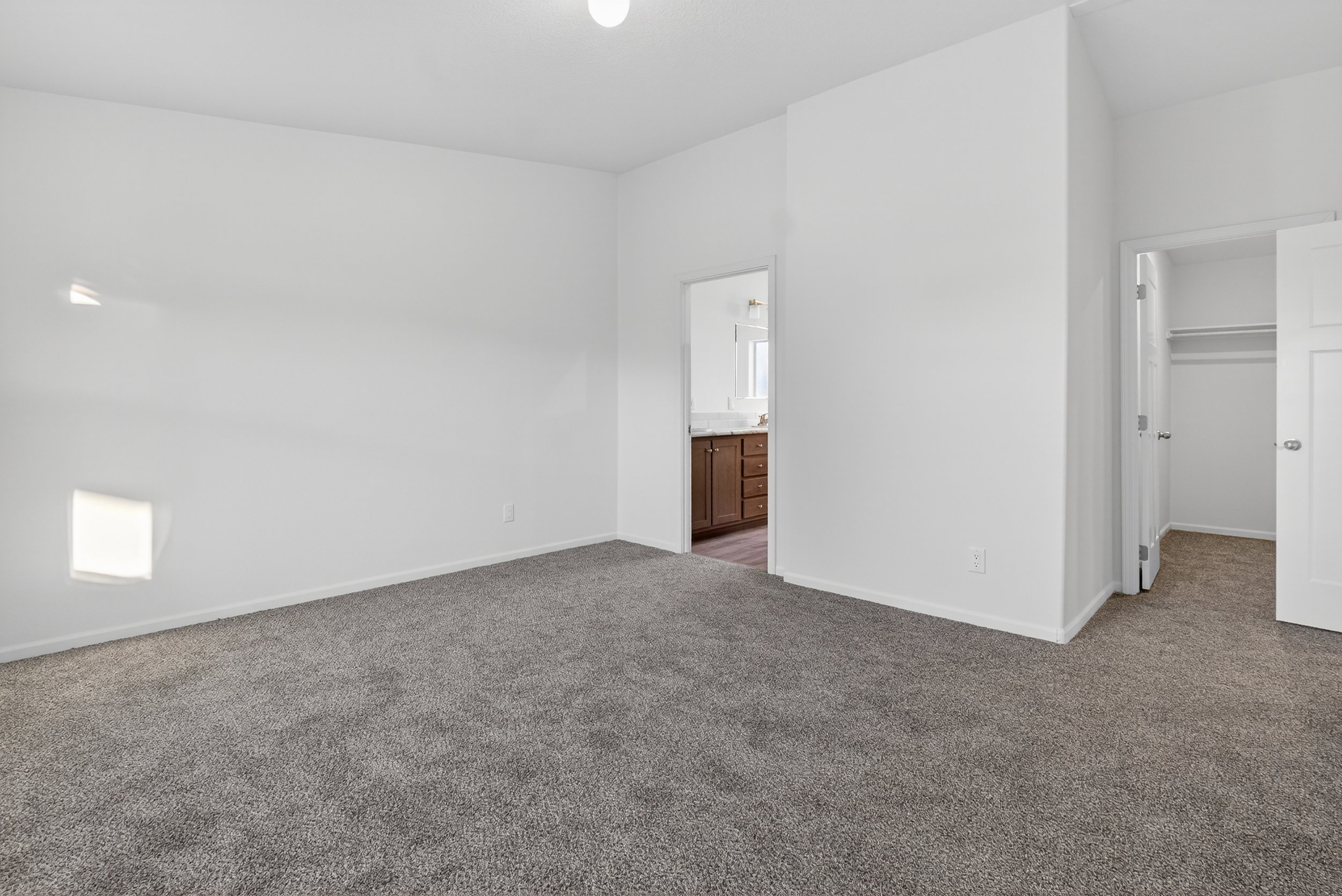 Unfurnished bedroom featuring a spacious closet, dark colored carpet, and ensuite bath