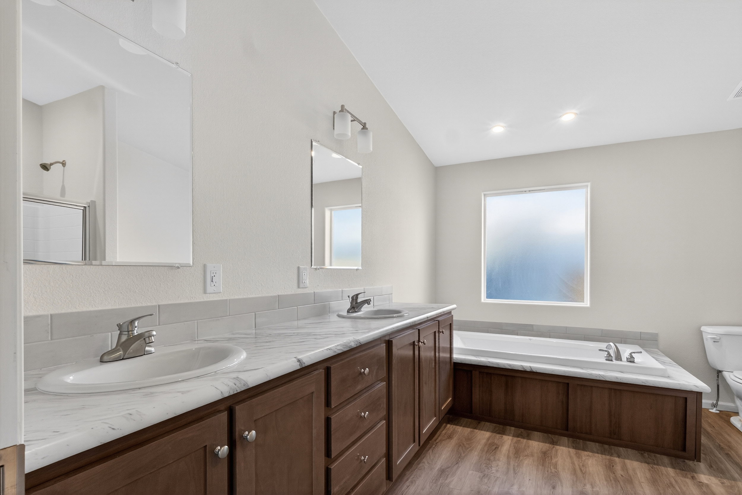 Full bathroom featuring double vanity, a garden tub, and light wood finished floors