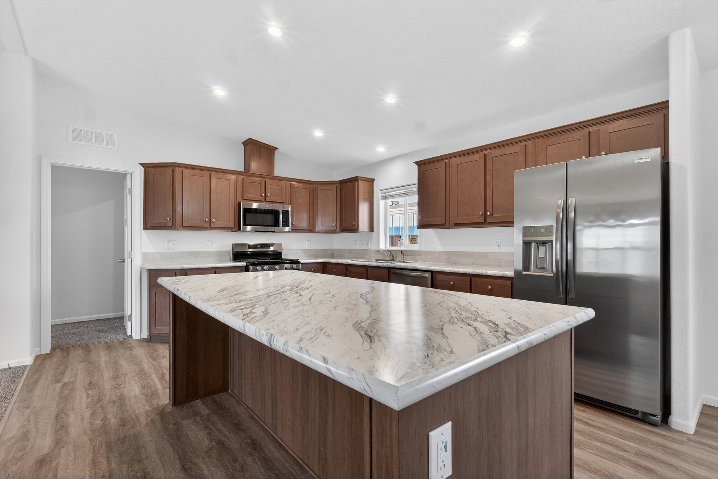 Kitchen with lofted ceiling, stainless steel appliances, a center island, light wood-style floors, and light stone counters