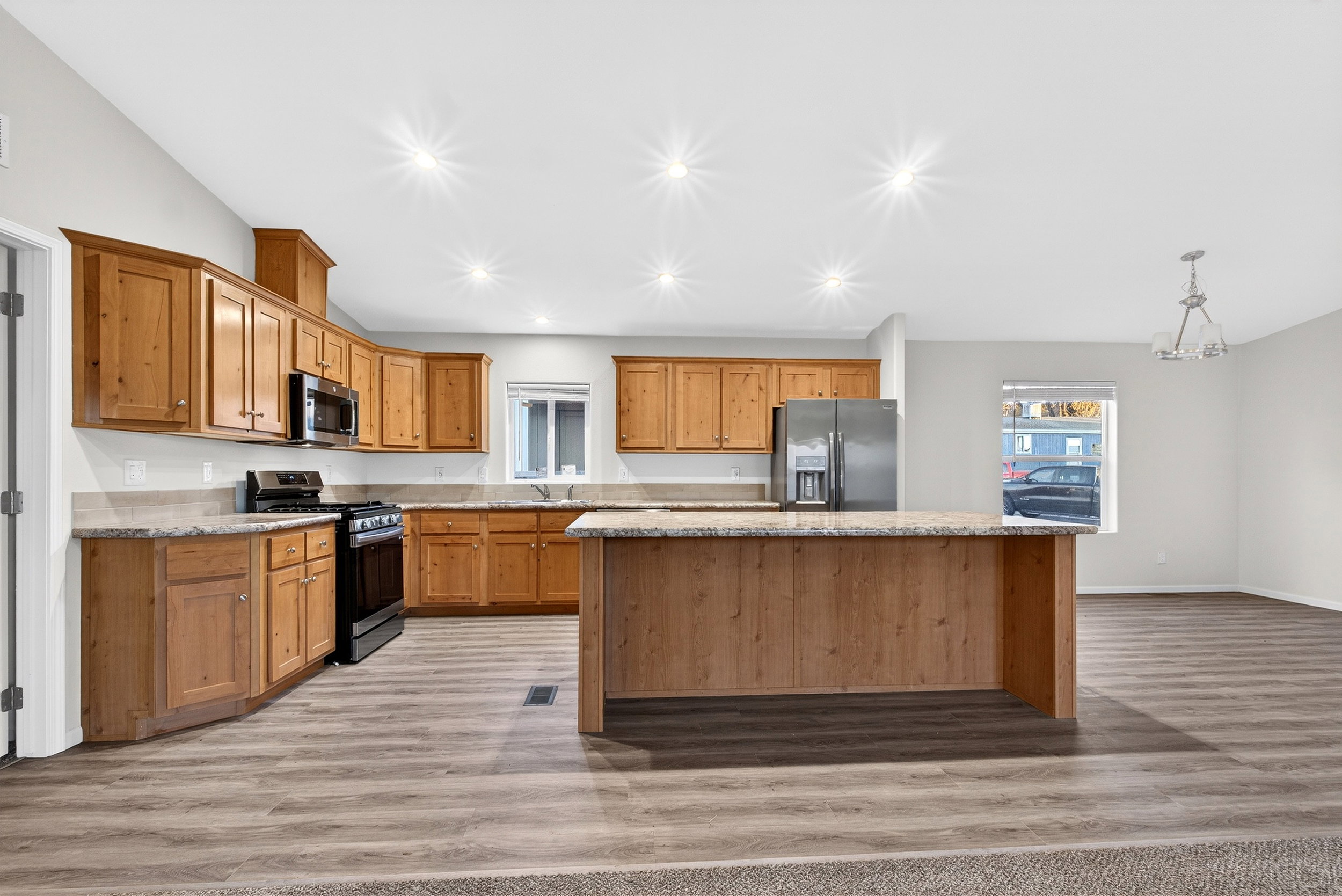Kitchen featuring stainless steel appliances, light stone counters, brown cabinets, pendant lighting, and a center island