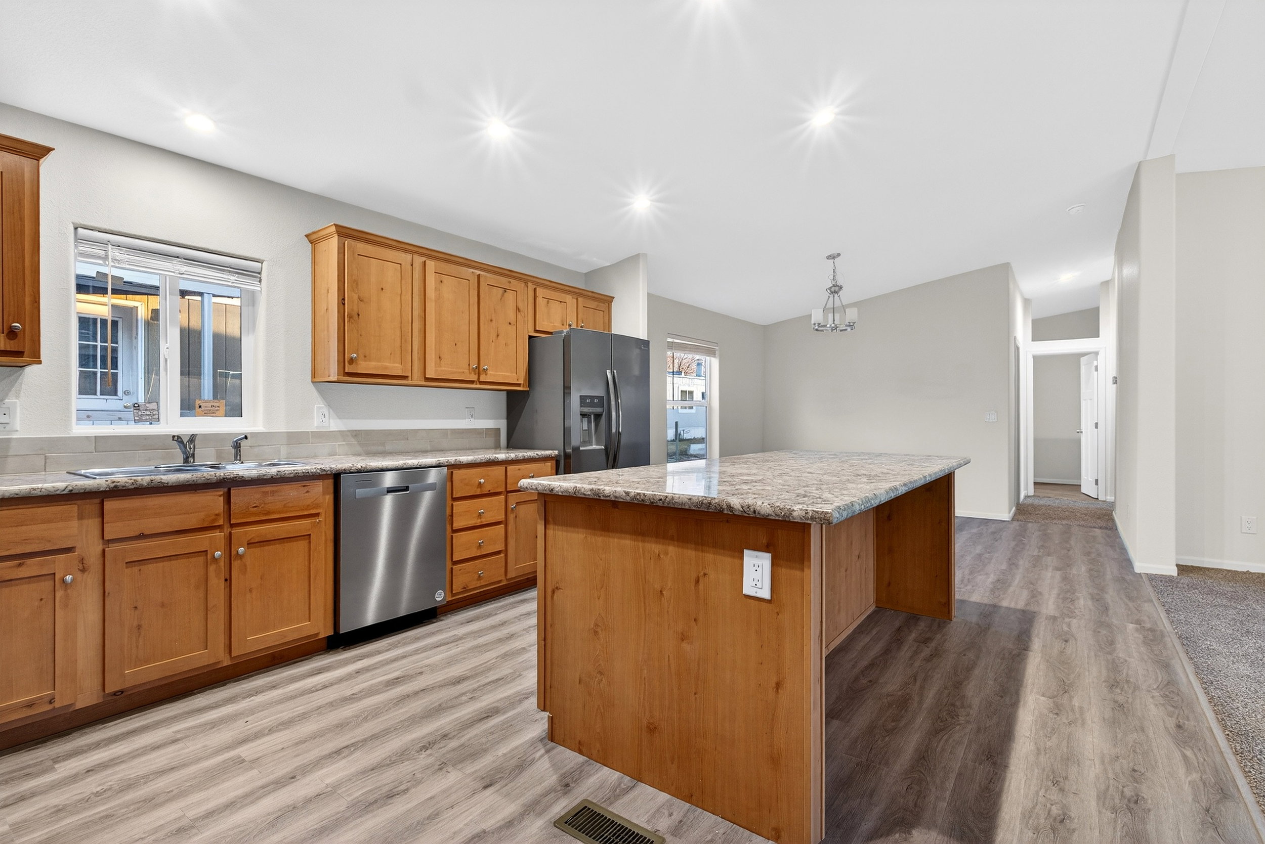 Kitchen featuring stainless steel dishwasher, black fridge, a center island, brown cabinetry, and light stone countertops