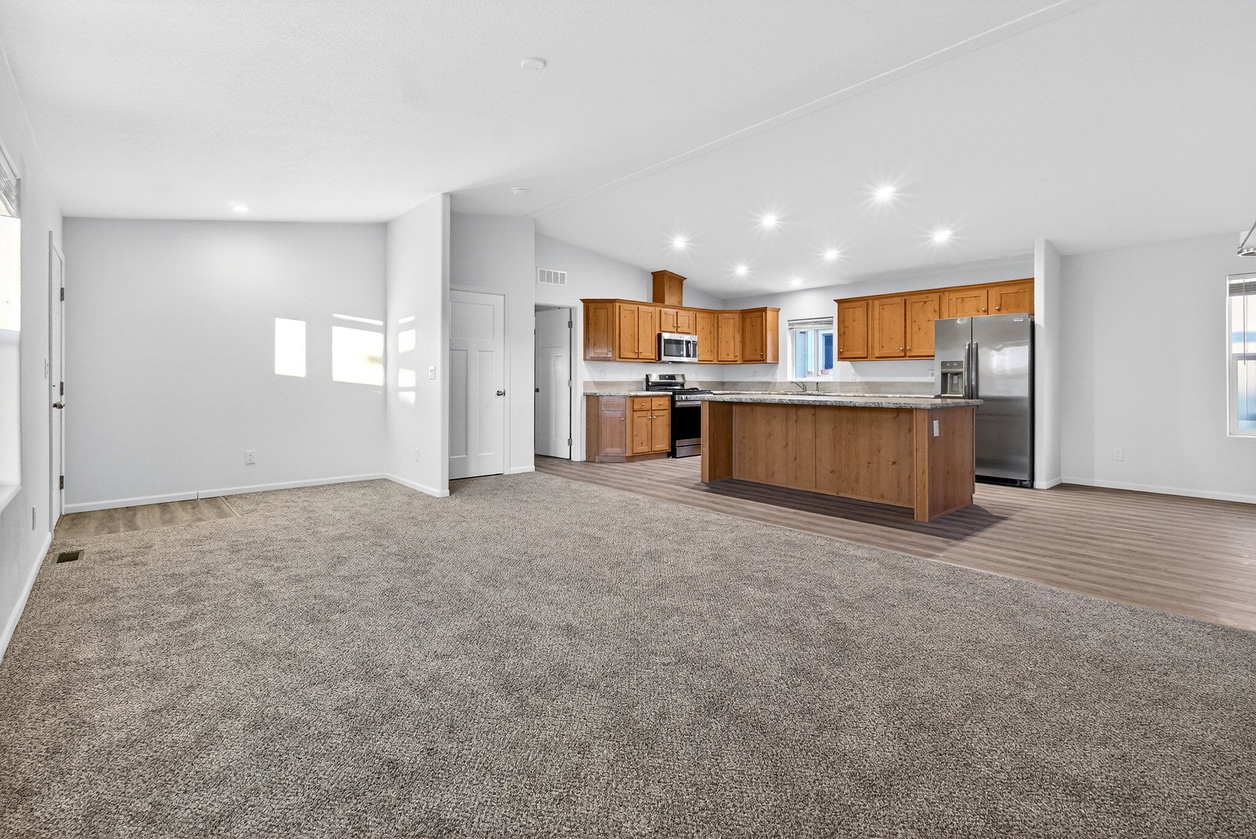 Kitchen with open floor plan, light carpet, brown cabinetry, appliances with stainless steel finishes, and lofted ceiling