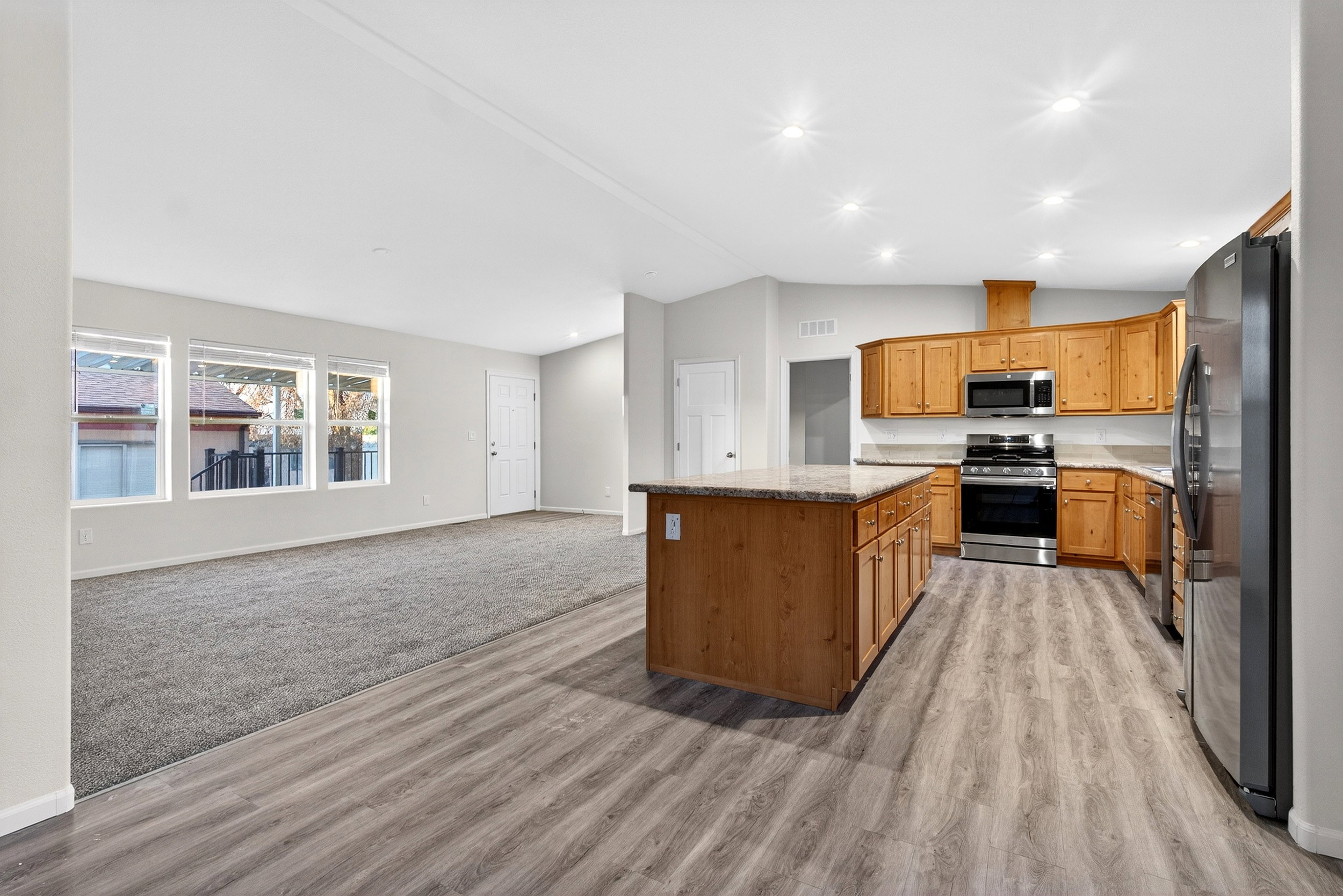 Kitchen with vaulted ceiling, stainless steel appliances, open floor plan, a center island, and light stone counters