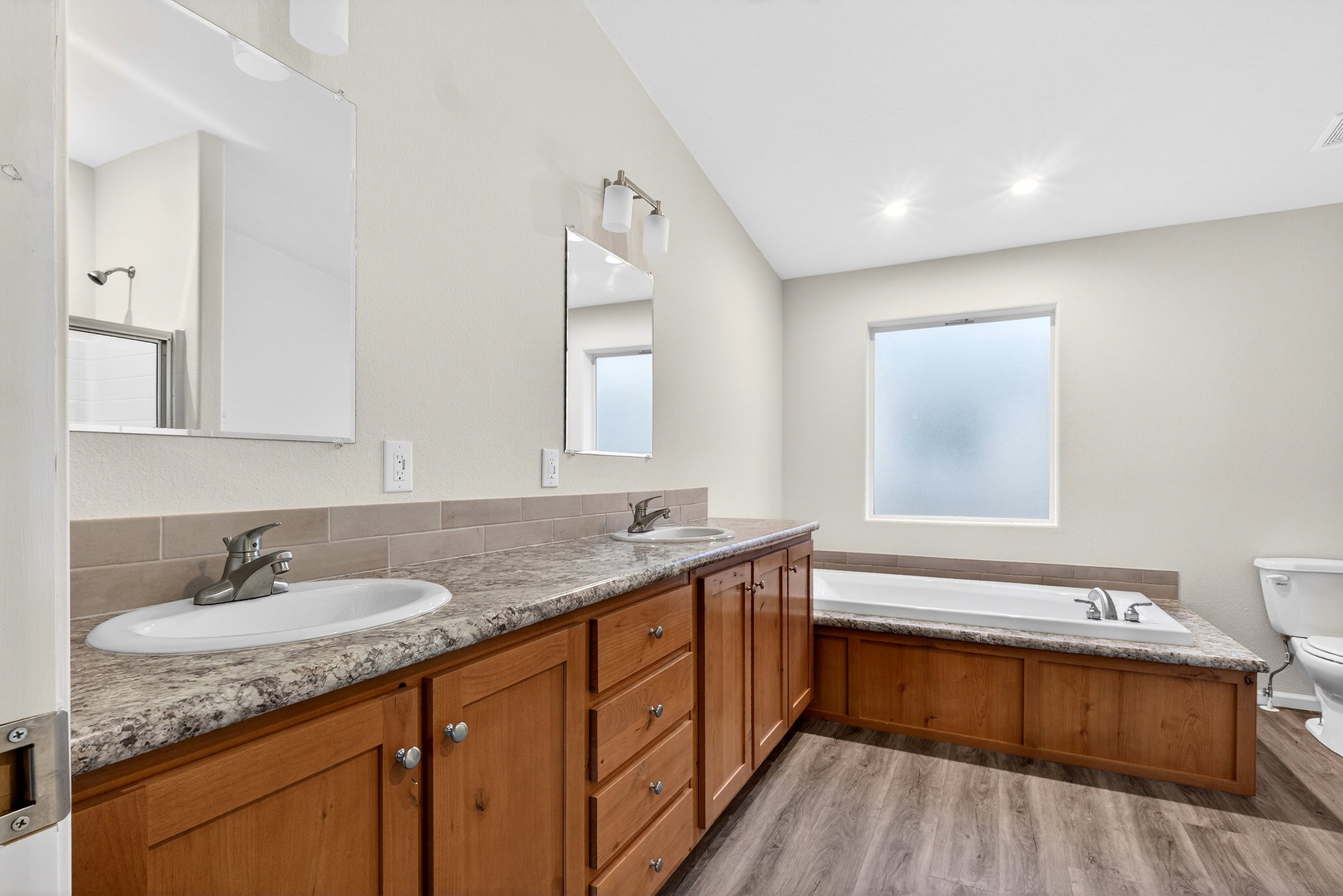 Full bath with a garden tub, double vanity, and light wood-style flooring