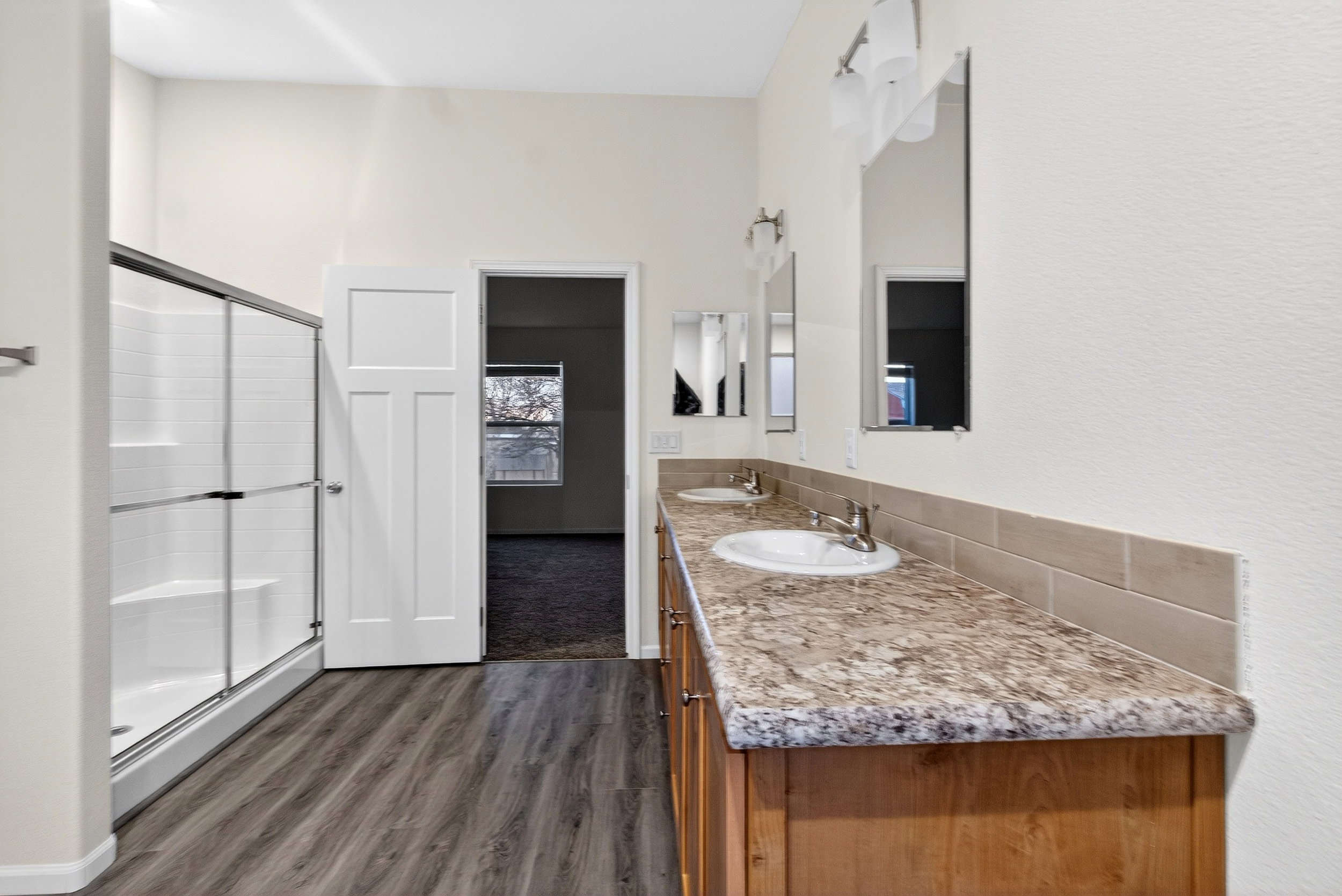 Full bathroom featuring double vanity, dark wood-type flooring, and a stall shower