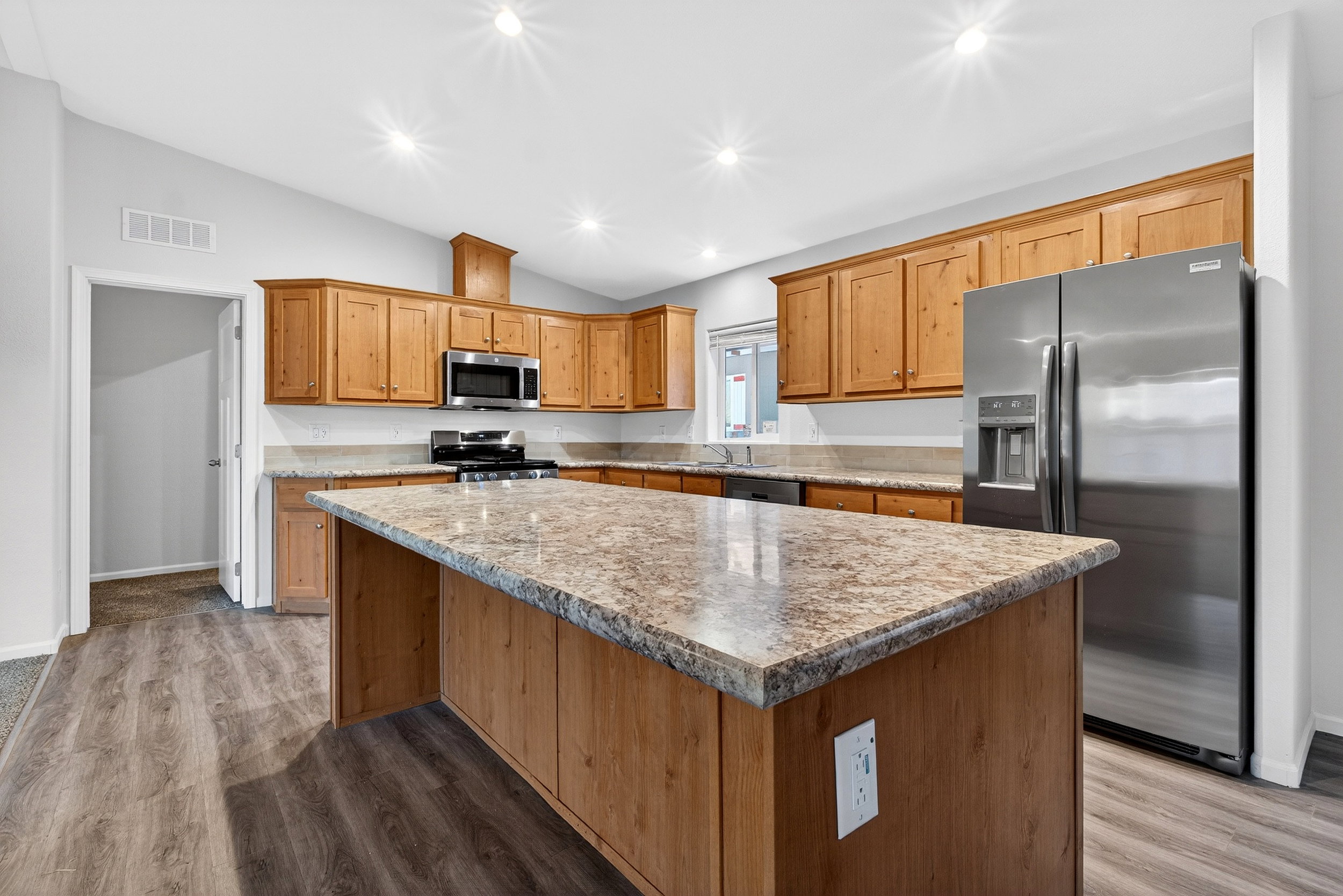 Kitchen with vaulted ceiling, appliances with stainless steel finishes, light stone counters, a center island, and recessed lighting