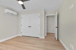 Unfurnished bedroom featuring a wall mounted air conditioner, light wood finished floors, a closet, and a ceiling fan