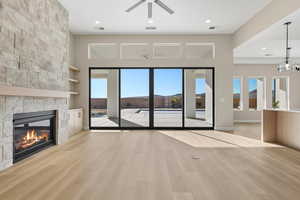 Unfurnished living room featuring light wood-type flooring, healthy amount of natural light, built in features, recessed lighting, and a stone fireplace