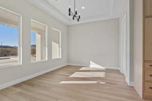 Unfurnished dining area featuring a chandelier, a raised ceiling, light wood-style flooring, plenty of natural light, and recessed lighting
