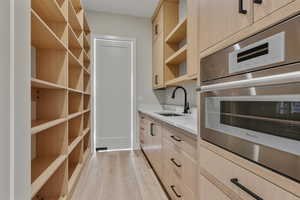 Kitchen with light brown cabinetry, open shelves, stainless steel oven, light wood-type flooring, and light stone countertops