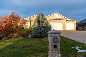 View of property hidden behind natural elements featuring concrete driveway, a front yard, an attached garage, and brick siding