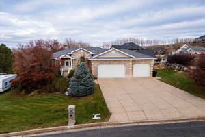 View of front facade featuring a front lawn, driveway, a garage, and stone siding