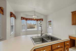 Kitchen featuring light countertops, brown cabinetry, decorative light fixtures, and lofted ceiling