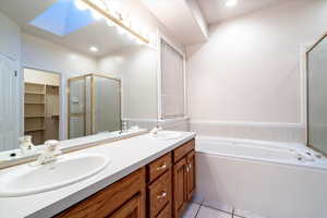 Full bathroom with double vanity, a spacious closet, a garden tub, a shower stall, and light tile patterned floors