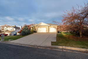 View of front of house featuring concrete driveway, a front lawn, a garage, and stone siding
