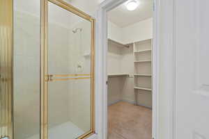 Bathroom featuring light colored carpet, a shower stall, and a walk in closet