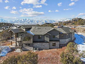 Snow covered property featuring stone siding, a mountain view, stairs, a sunroom, and roof with shingles