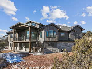 Rear view of house with stairs, a patio, stone siding, and a balcony