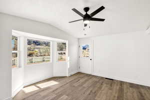 Empty room with wood finished floors, vaulted ceiling, and ceiling fan