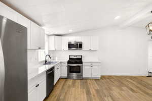 Kitchen featuring appliances with stainless steel finishes, white cabinetry, light wood-style flooring, lofted ceiling, and recessed lighting