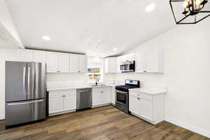 Kitchen with stainless steel appliances, white cabinets, light countertops, a chandelier, and vaulted ceiling