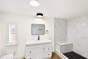 Full bath featuring vanity, a marble finish shower, and light wood-style floors