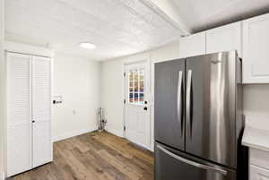 Kitchen with freestanding refrigerator, white cabinets, dark wood-style flooring, a textured ceiling, and light stone countertops