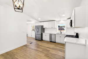 Kitchen featuring white cabinetry, appliances with stainless steel finishes, light wood-style flooring, recessed lighting, and lofted ceiling