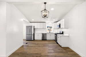 Kitchen with white cabinetry, appliances with stainless steel finishes, vaulted ceiling, dark wood-type flooring, and decorative light fixtures