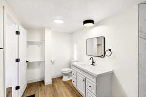 Full bath with a textured ceiling, vanity, a spacious closet, and light wood-style floors