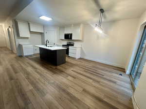 Kitchen with white cabinetry, stainless steel appliances, a kitchen island with sink, light wood finished floors, and decorative light fixtures