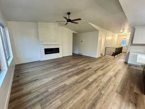 Unfurnished living room featuring light wood finished floors, lofted ceiling, a large fireplace, and ceiling fan