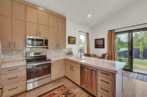 Kitchen with light brown cabinets, stainless steel appliances, light stone countertops, lofted ceiling, and backsplash