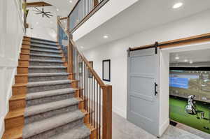 Stairs with a barn door, a high ceiling, carpet flooring, recessed lighting, and golf simulator