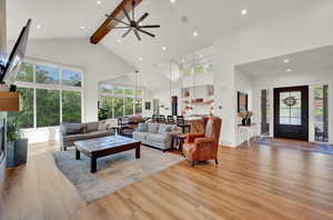 Living room with a glass covered fireplace, high vaulted ceiling, light wood-style floors, ceiling fan, and beamed ceiling