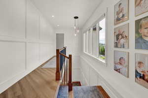 Hall with a decorative wall, an upstairs landing, light wood-type flooring, and recessed lighting