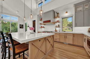 Kitchen featuring light brown cabinetry, plenty of natural light, decorative light fixtures, open shelves, and high vaulted ceiling